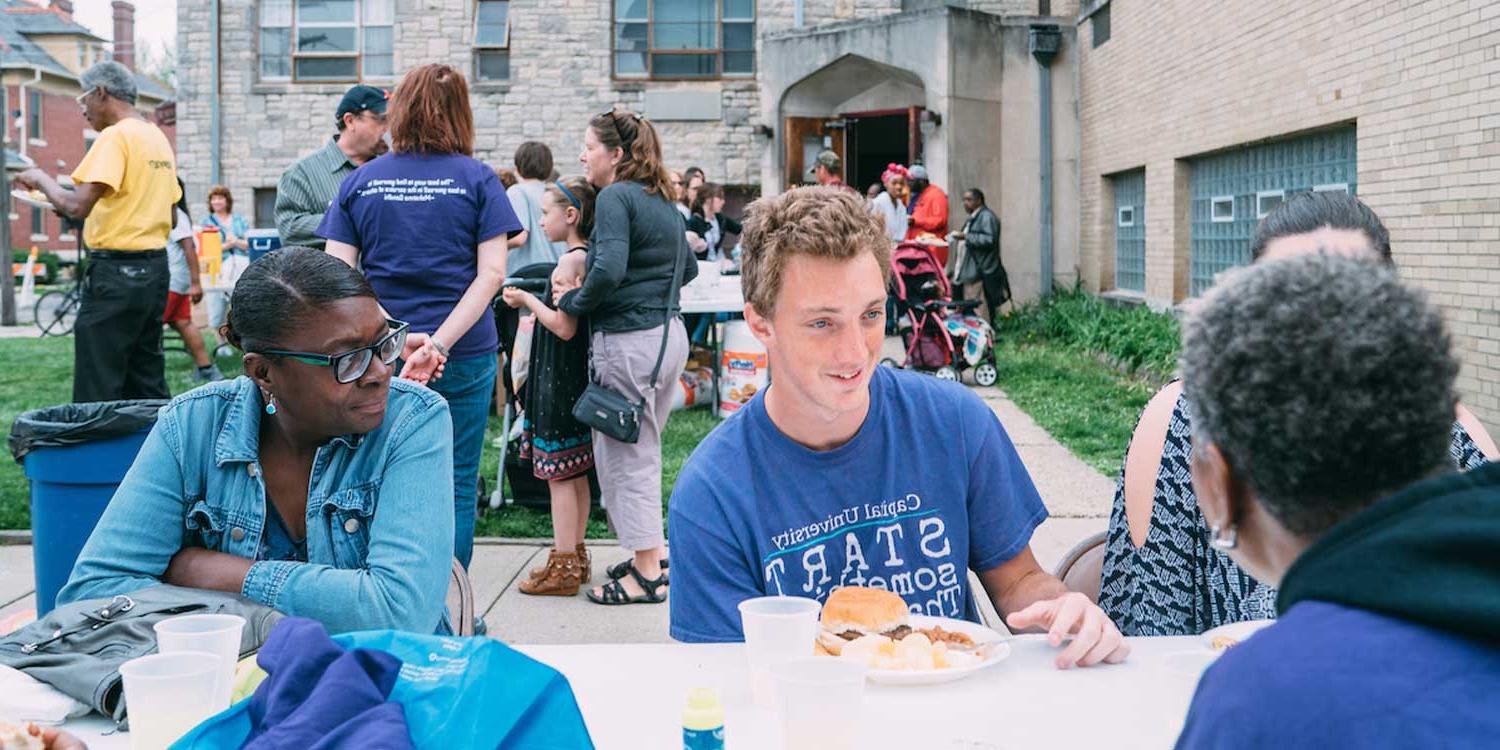 在一个街区聚会上，万博的学生在外面的野餐桌上吃饭